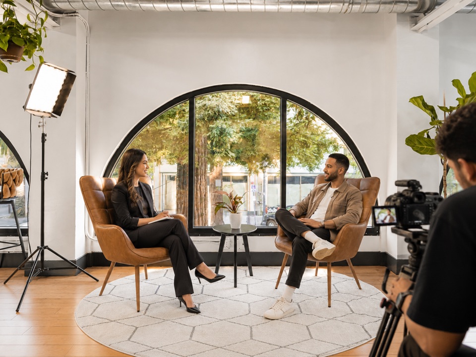 A filmed interview set up beside an arched window, with lighting and camera gear